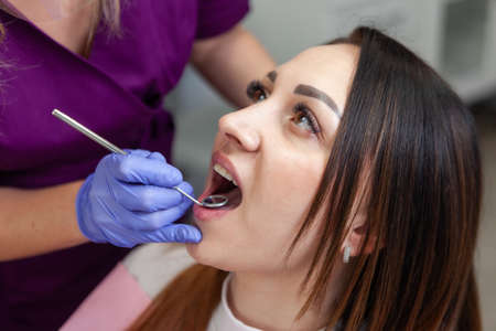 Young woman being examined by the stomatologist. Beauty female sitting in medical chair while dentist fixing her teeth at dental clinic. Dentist examining patient's teethの写真素材