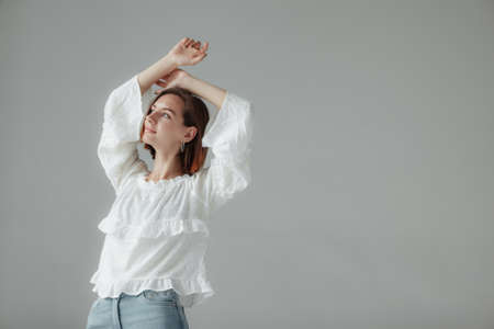 Stylish woman in a white blouse and jeans on a gray background. Grace and femininity concept