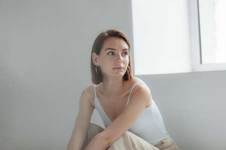 Young stylish woman sitting by a light window in a white roomの写真素材