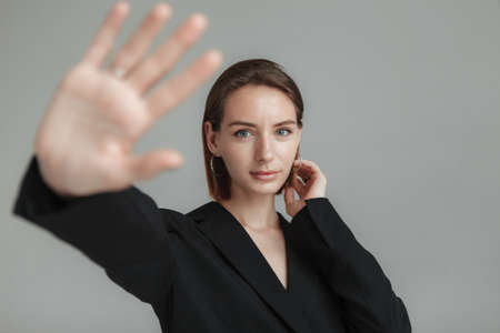 Young stylish woman showing stop sign with hand on gray background. stop abuse