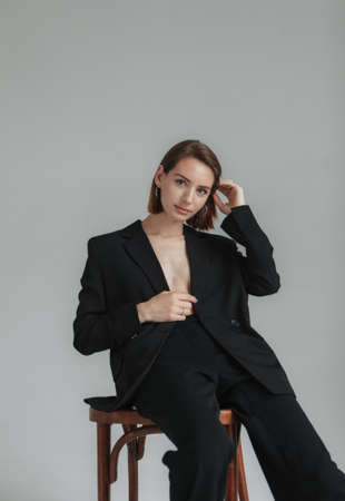 Sexy young woman in a jacket on a naked body and trousers sitting on chair in the studio. fashion shotの写真素材