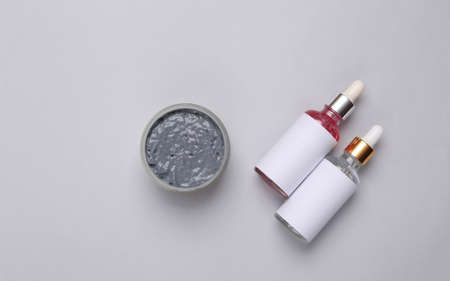 Bottles of face serum and a jar of black clay on gray background. flat layの写真素材