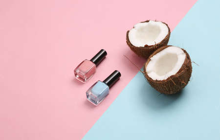 Nail polish bottles and coconut on blue pink background