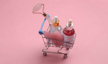 Mini shopping cart with face skin care products on pink backgroundの写真素材