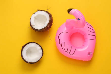 Inflatable flamingo with coconut on a yellow background. Minimal summer vacation concept. top view
