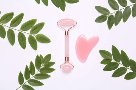 Face roller and gua sha stone massager on white background with green leaves. top viewの写真素材