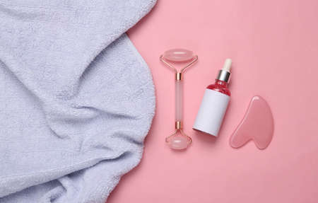 Massage roller with a bottle of facial serum and a towel on a pink background. Facelift, anti-aging massageの写真素材