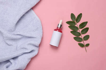 Bottle of face serum with sprigs of green leaves and towel on a pink background. natural cosmetics...