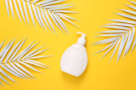 White cream bottle with palm leaves on yellow background.