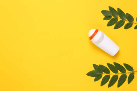 Antiperspirant roller with green leaves on yellow background. top viewの写真素材