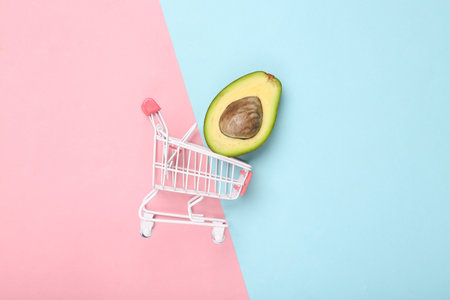Mini supermarket trolley with half ripe avocado on blue pink pastel backgroundの写真素材