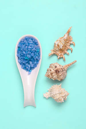 Ceramic spoon with sea salt for bath and seashells on blue background. top view