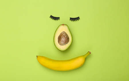 Creative face shape composition made of false eyelashes, avocado and banana on green backgroundの写真素材