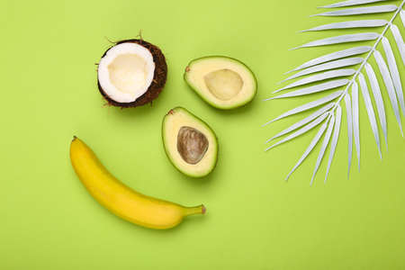 Half avocado and coconut, banana on green background with palm leaves. Creative tropical fruit...