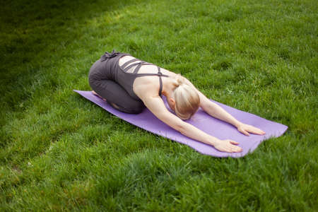 Young attractive blonde woman practicing yoga asana pose while sitting on the mat in the parkの写真素材