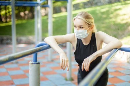 Portrait of young fit woman in medical mask on workout ground