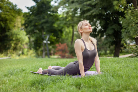 Young attractive blonde woman practicing yoga asana pose on the mat in the parkの写真素材