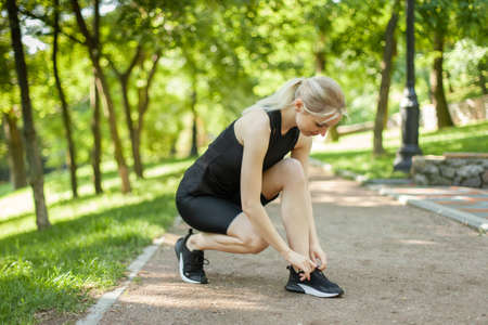 Young fit woman tying the laces of sneakers in the park