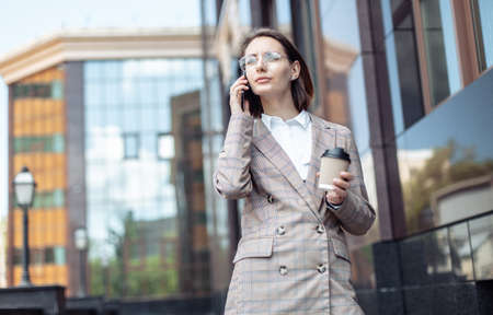 Young modern business lady talking on the phone and drinking coffee on the go.の写真素材