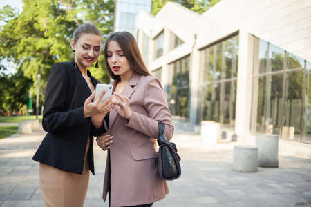 Two smiling business women looking at smartphone screen outdoorsの写真素材