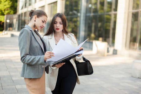 Two young business women carefully study a folder with documents in the cityの写真素材
