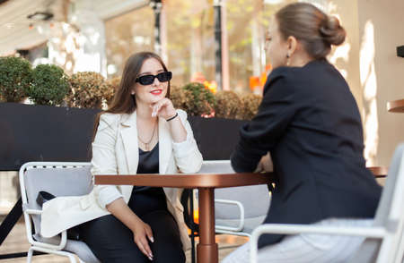Two cute women friend talking while discussing while sitting at table in outdoor cafeの写真素材