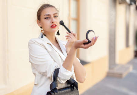 Young beautiful caucasian woman applying makeup with a brush in the cityの写真素材