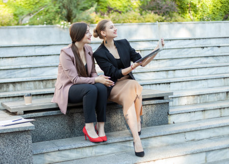 Two business women sitting on bench with laptop in the parkの写真素材