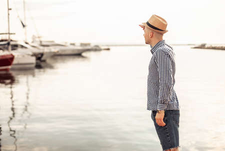 Young man with hat looks into the distance on the background of the yacht clubの写真素材