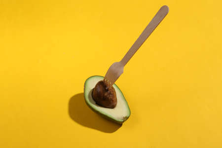 Minimal summer still life. Half an avocado with wooden fork on bright yellow background. creative eco layoutの写真素材