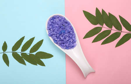 spa therapy. Spoon with bath salt on a blue-pink pastel background with green leaves. top view