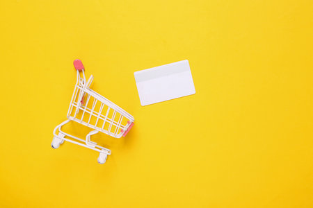 Mini shopping cart with bank card on yellow background. top viewの写真素材
