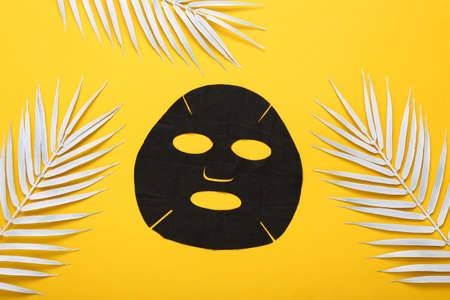 Black cosmetic cleansing mask with white palm leaves on yellow backgroundの写真素材