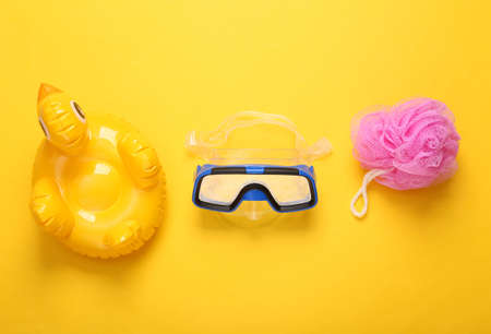 Children's accessories and toys for bathing. Diving mask, duck and washcloth on yellow background....