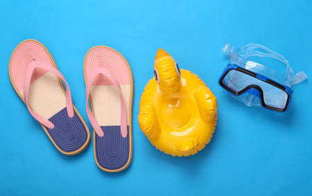 Summer holidays. Diving mask and inflatable duck, flip flops on blue pink pastel background. Minimal...