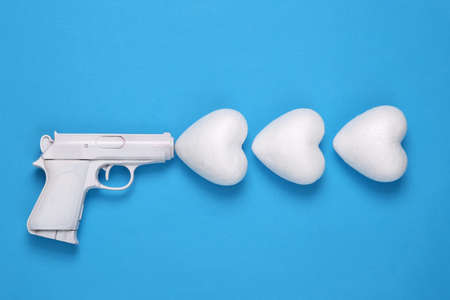White gun with heart on blue background. Minimal, creative layout, love concept, top view