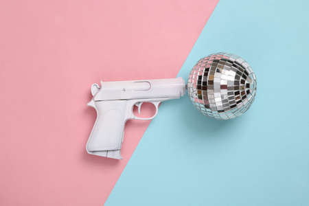 Gun with disco ball on pink blue background. party concept. creative minimal layout. top viewの写真素材