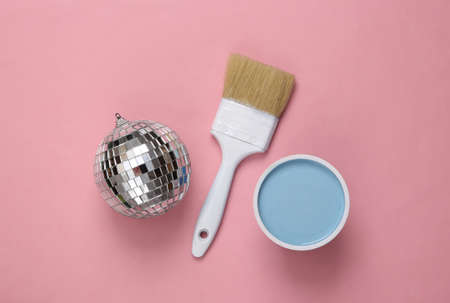 Disco ball and paint jar with paintbrush on pink background. top view