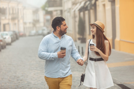 International couple in love drinking coffee walking around the city, holding handの写真素材