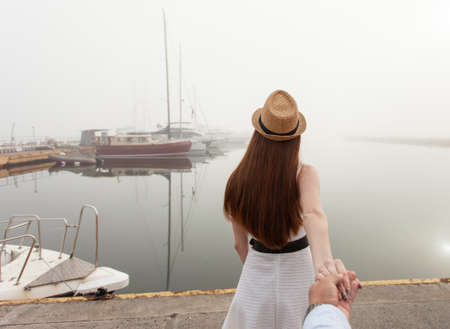 follow me. Woman tourist holds the hand of a guy in a yacht club in the fog