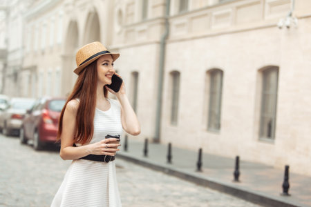 Cute caucasian woman in hat talking on the phone and drinking coffee in the cityの写真素材
