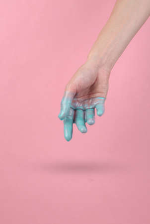 Human hand with dripping turquoise paint on a pink background. minimal creative layout. concept artの写真素材