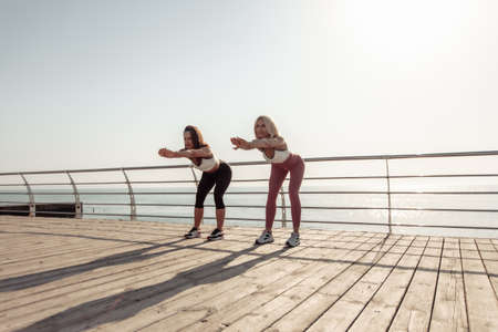 Two athletic women warming up doing exercises early morning on the beachの写真素材