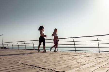 Two athletic women friends running along the embankment in the early morningの写真素材