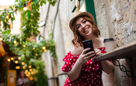 Young stylish woman in polka dot dress uses smartphone in street cafeの写真素材