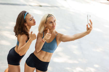 Two beautiful athletic women take selfie on smartphone outdoorsの写真素材