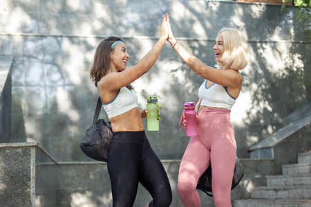 Two beautiful athletic women in sportswear with perfect body high five to each other outdoorsの写真素材