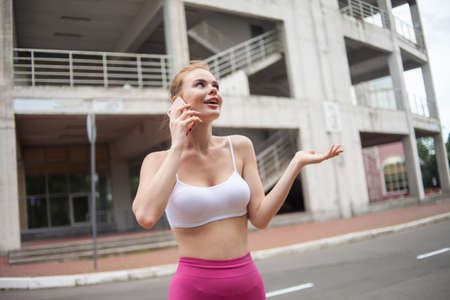 Young emotional fitness woman in sportswear talking on the phone in a city locationの写真素材
