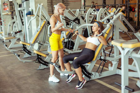 Fit woman and her trainer doing exercise at the gym. Personal trainer Coordinates woman training in...
