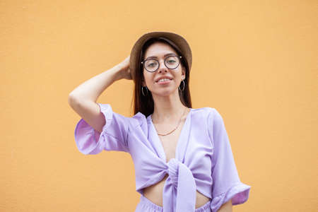 Portrait of young stylish woman in hat and glasses on yellow backgroundの写真素材